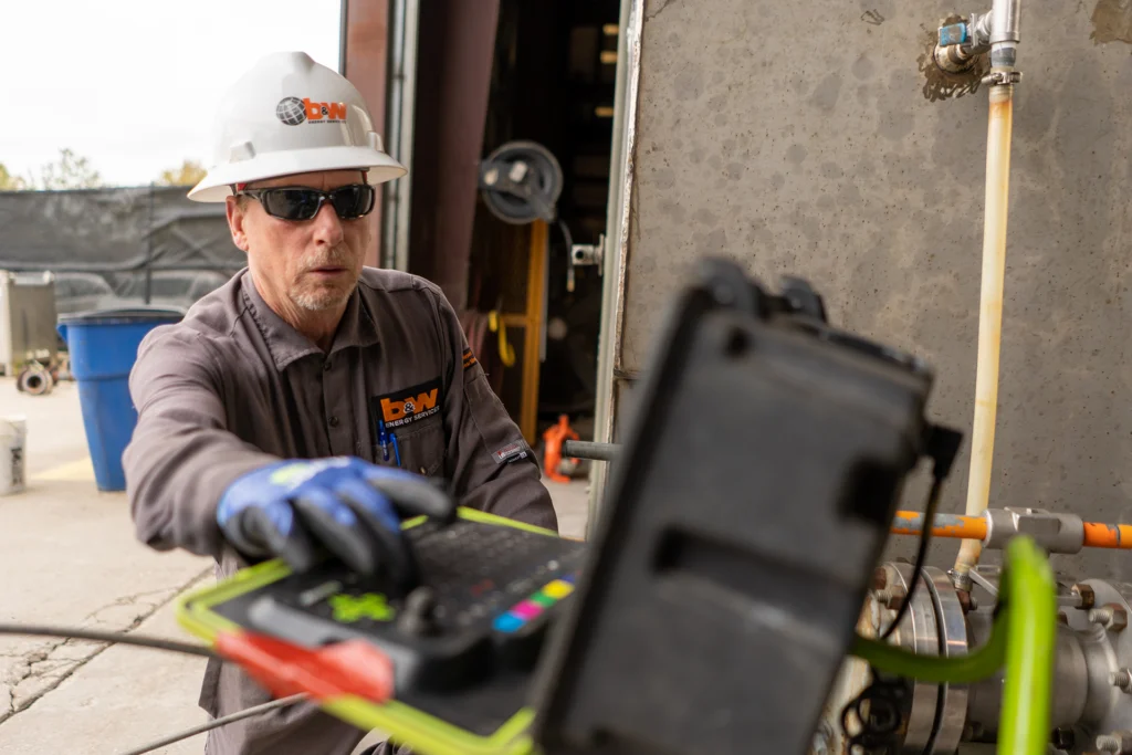 A technician wearing safety gear and sunglasses operates equipment outdoors.