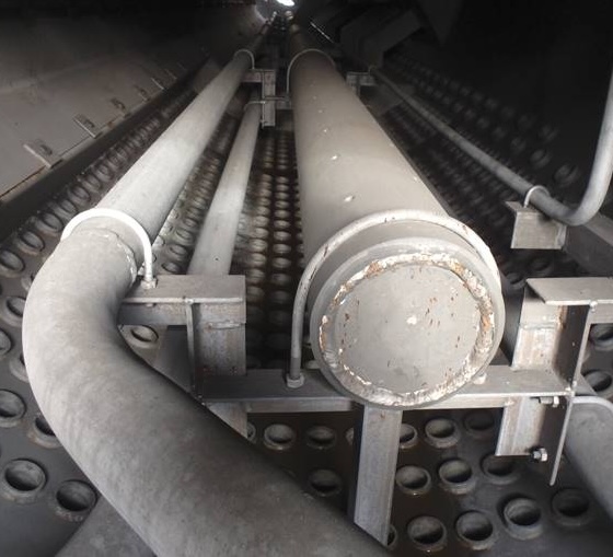 Interior view of an industrial tank with chemically cleaned metal pipes and a textured grid-like floor.